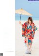 A woman in a kimono holding an umbrella on the beach.