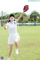 A woman in a white dress throwing a baseball glove.