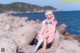 A woman in a bikini sitting on a rock by the ocean.