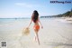 A woman in an orange bikini walking on the beach.