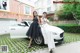 A couple of women standing next to a white car.